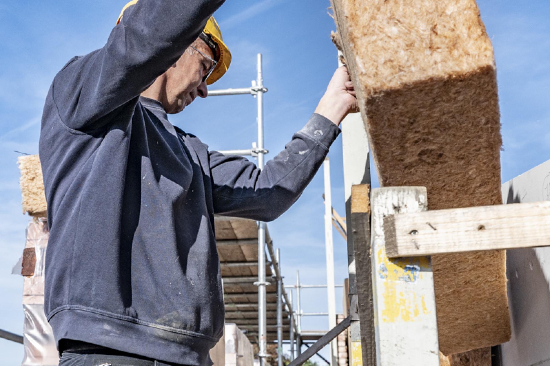 Man die bij een huis in aanbouw isolatiemateriaal aanbrengt