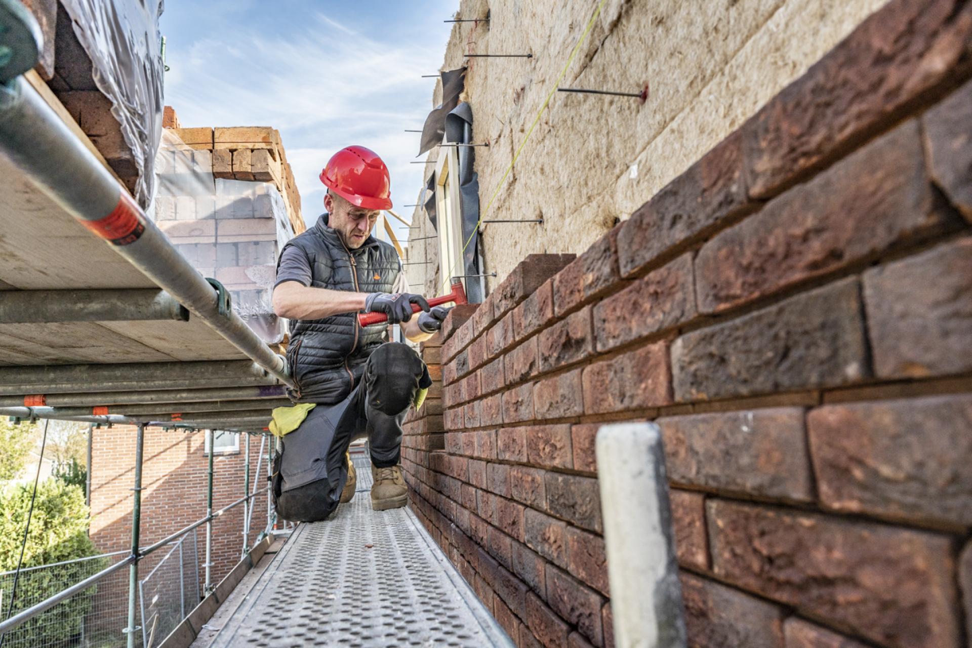 Man op steiger die stenen metselt