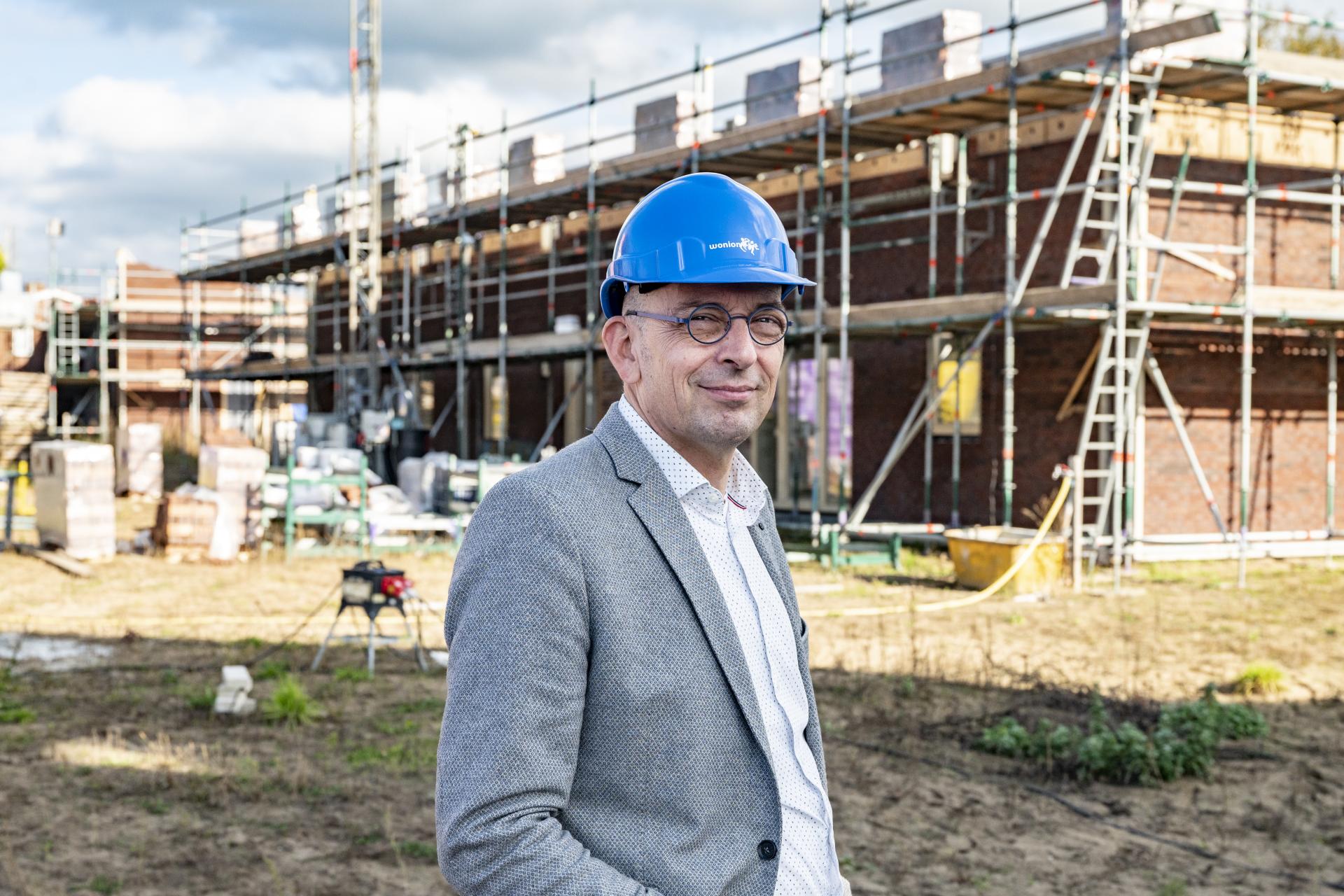 Man in pak met blauwe helm voor een bouwplaats met huizen in aanbouw
