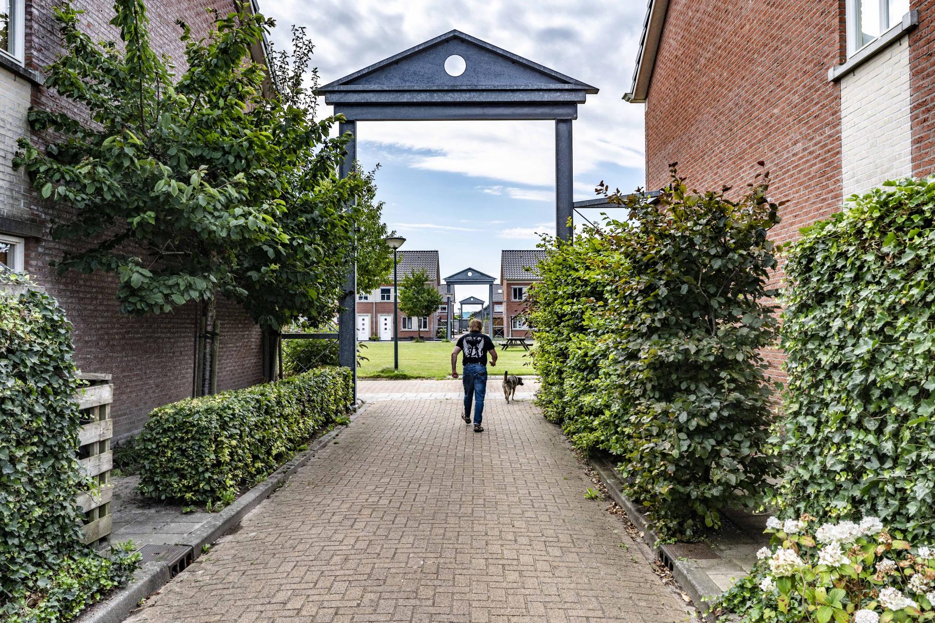 Een man die zijn hond uitlaat, loopt onder een poort door in een woonwijk.