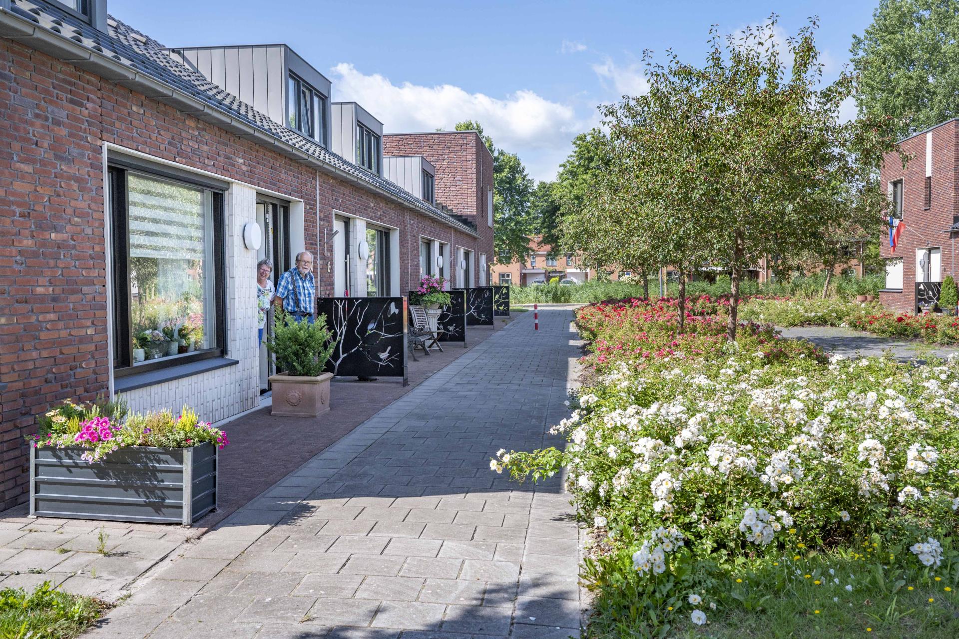  Een ouder echtpaar staat in de deuropening van hun woning.